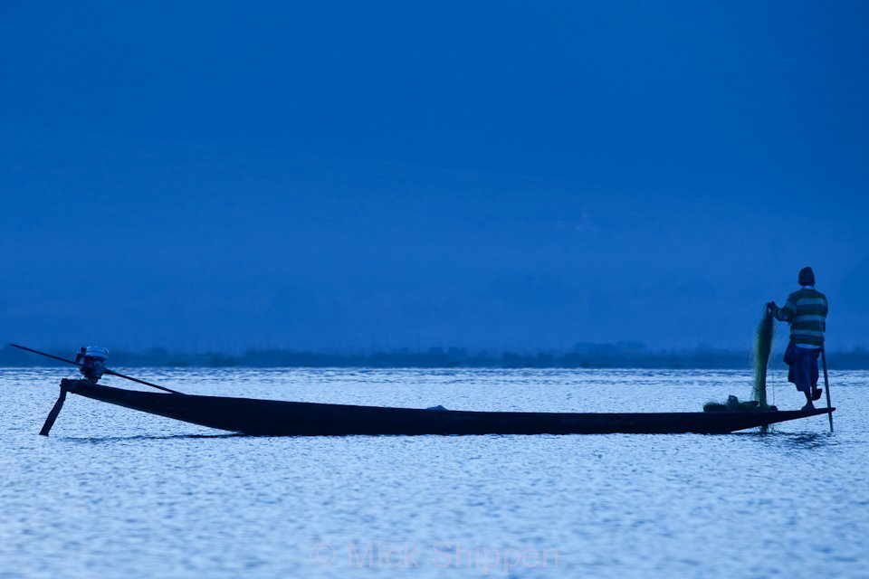 A fisherman on the lake  at dusk about to cast his nets.