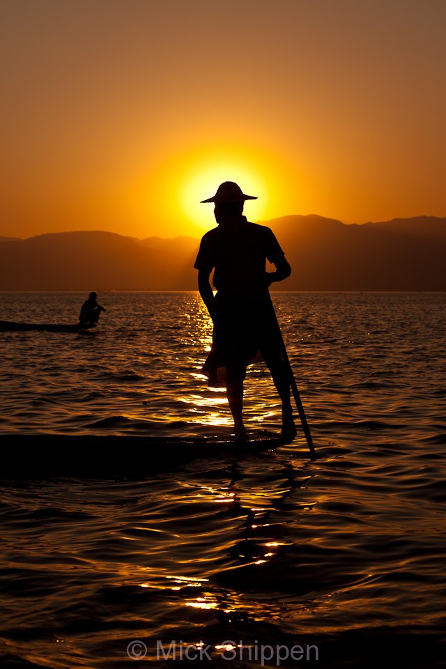 Leg rowing fishermen on the lake silhoutted against the setting sun.